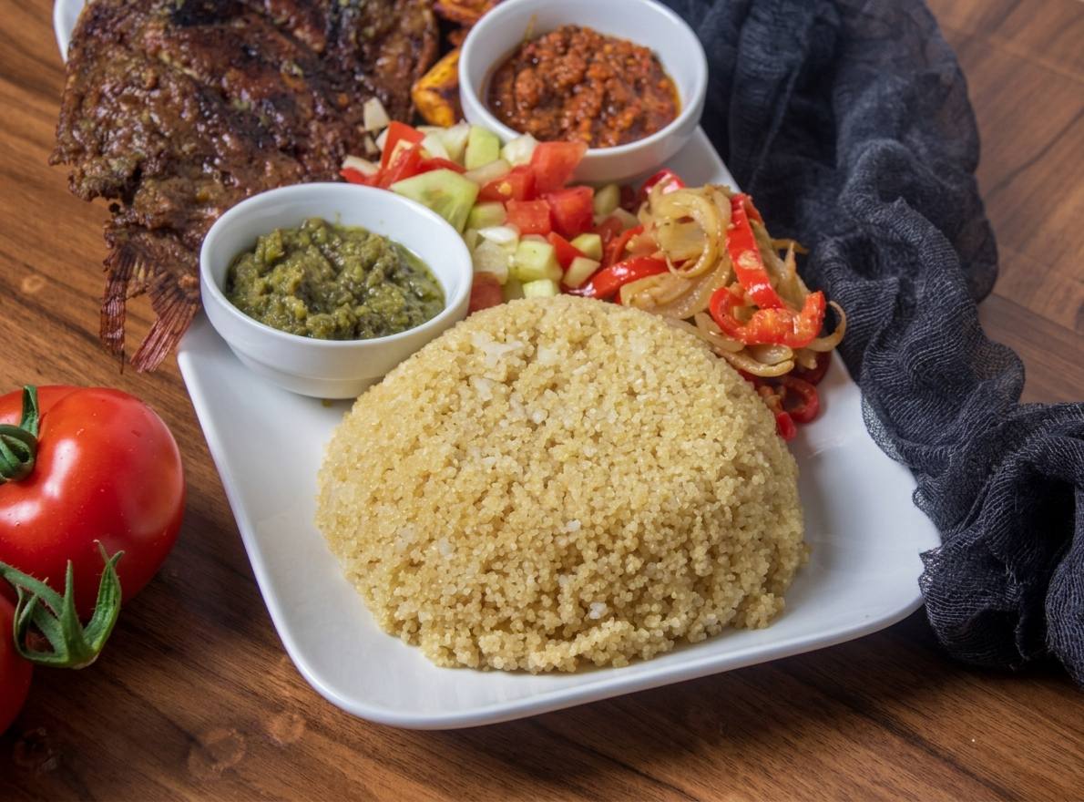 Domed mound of pale-yellow akyeke with whole grilled fish, red and green pepper sauces, tomato, cucumber and onion, Esiama